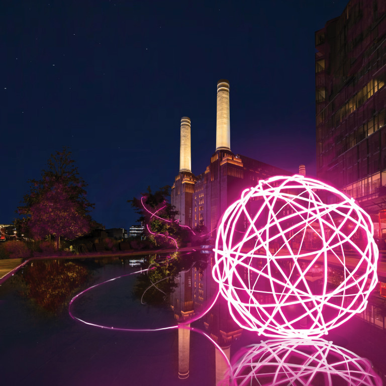 A glowing pink light installation reflecting on water with the iconic Battersea Power Station illuminated in the background.