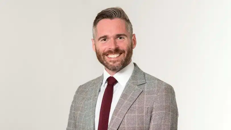 Professional portrait of Tom Copley - Deputy Mayor of London, wearing a grey suit and red tie, representing London leadership.
