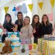 Smiling friends celebrate a baby shower London, surrounded by gifts, decorations, and a diaper cake in a bright, festive setting.