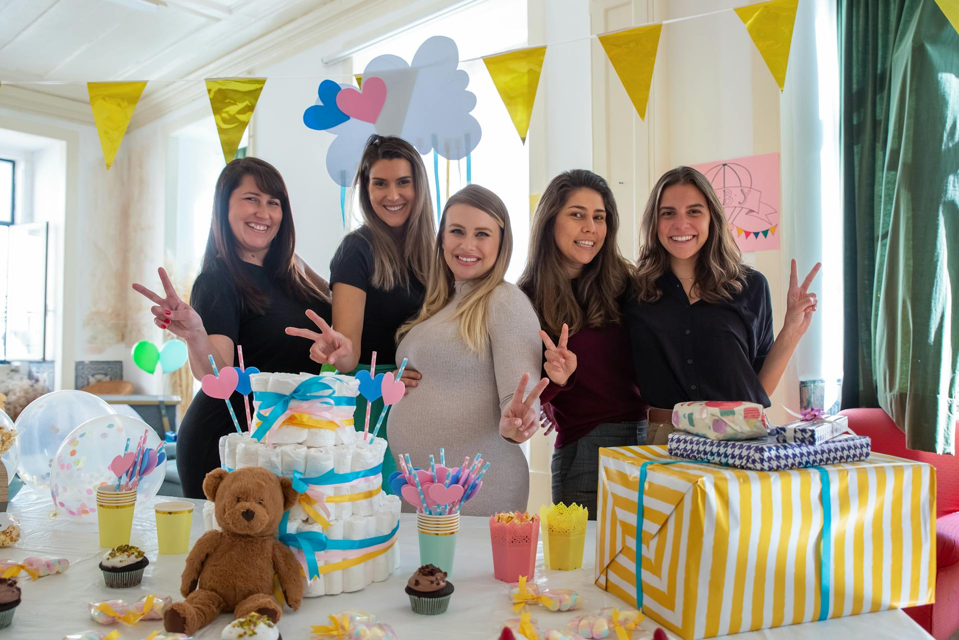 Smiling friends celebrate a baby shower London, surrounded by gifts, decorations, and a diaper cake in a bright, festive setting.